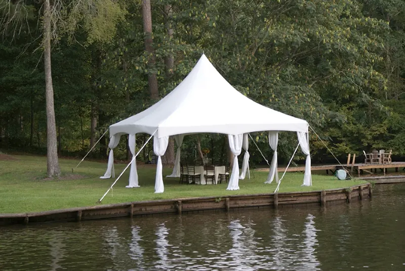 White frame tent tied down next to a lake
