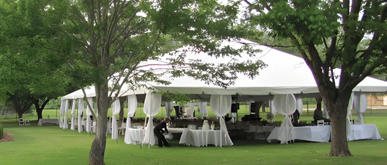 A big white frame tent that is being used for an event surrounded by trees.